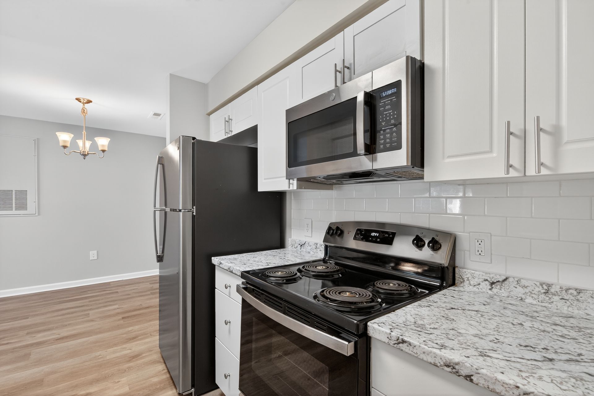 Modern kitchen with stainless steel appliances, white cabinets, granite counters, and light wood flooring