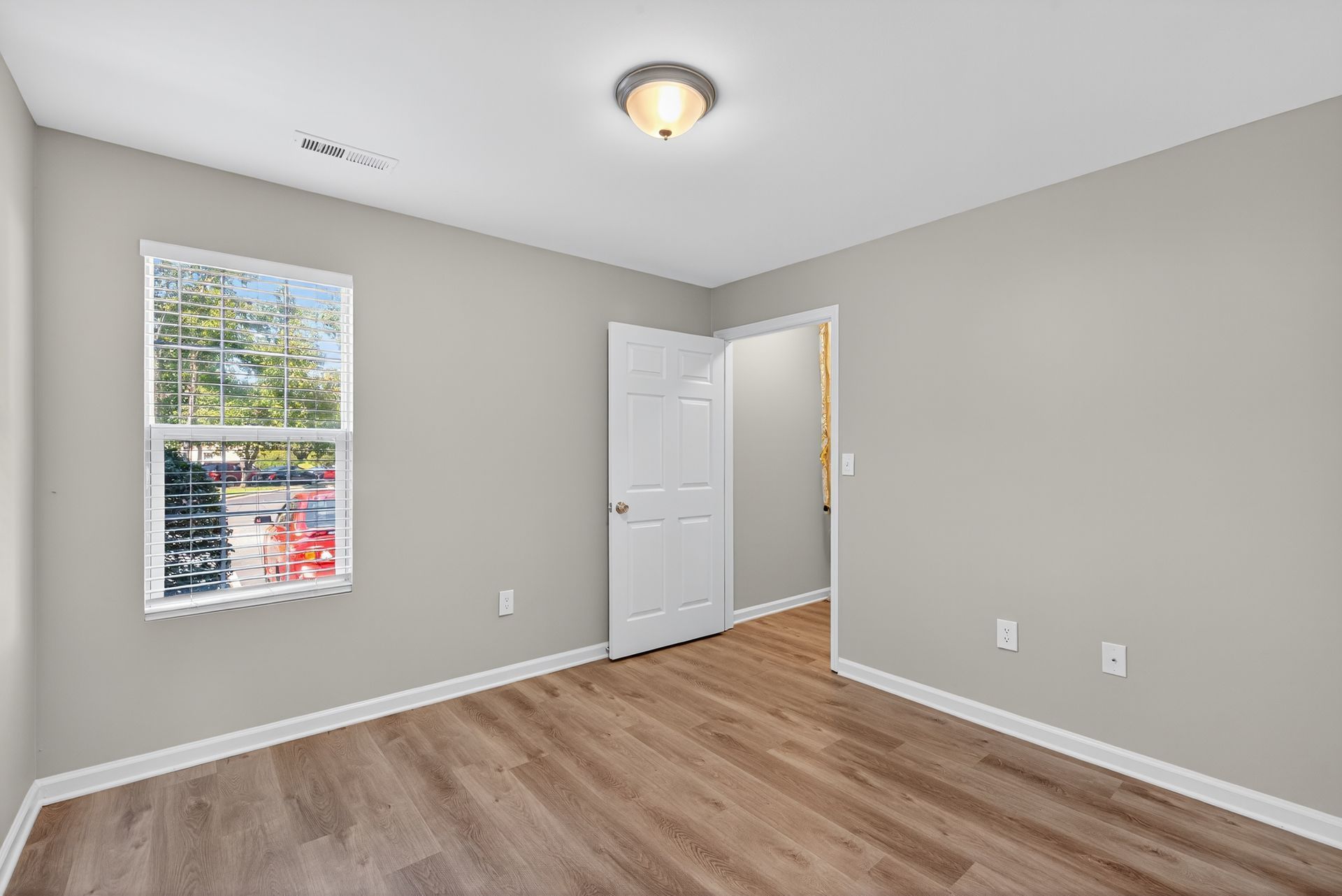 Empty beige bedroom with wood flooring, window, and open white closet door