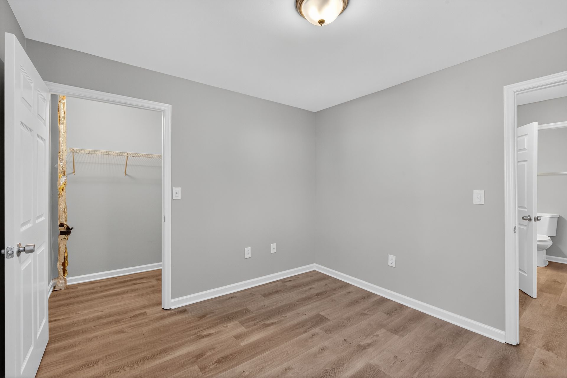Empty gray bedroom with wood-look floor, open closet, and door to a bathroom.
