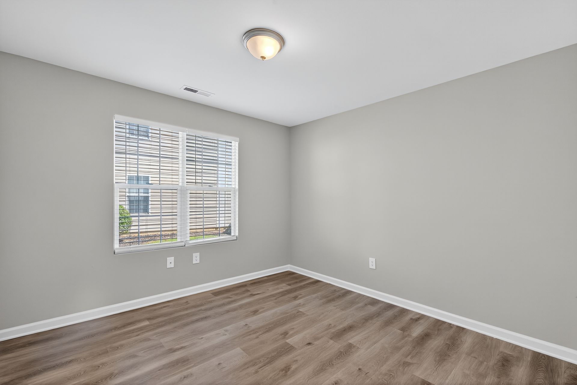 Empty gray bedroom with wood floors, window blinds, and a ceiling light