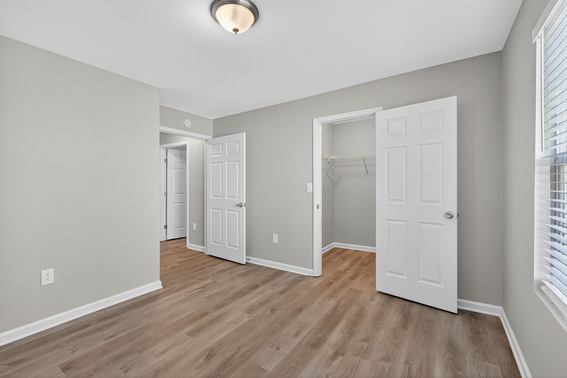 Empty bedroom with gray walls, wood flooring, white doors, and a closet.