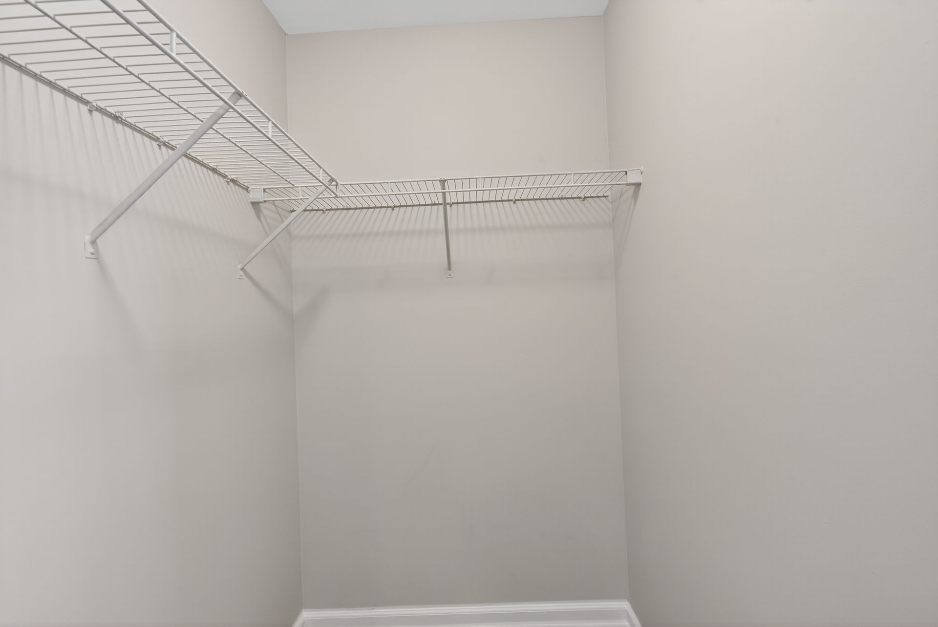 Empty white closet with wire shelving and hanging rods.