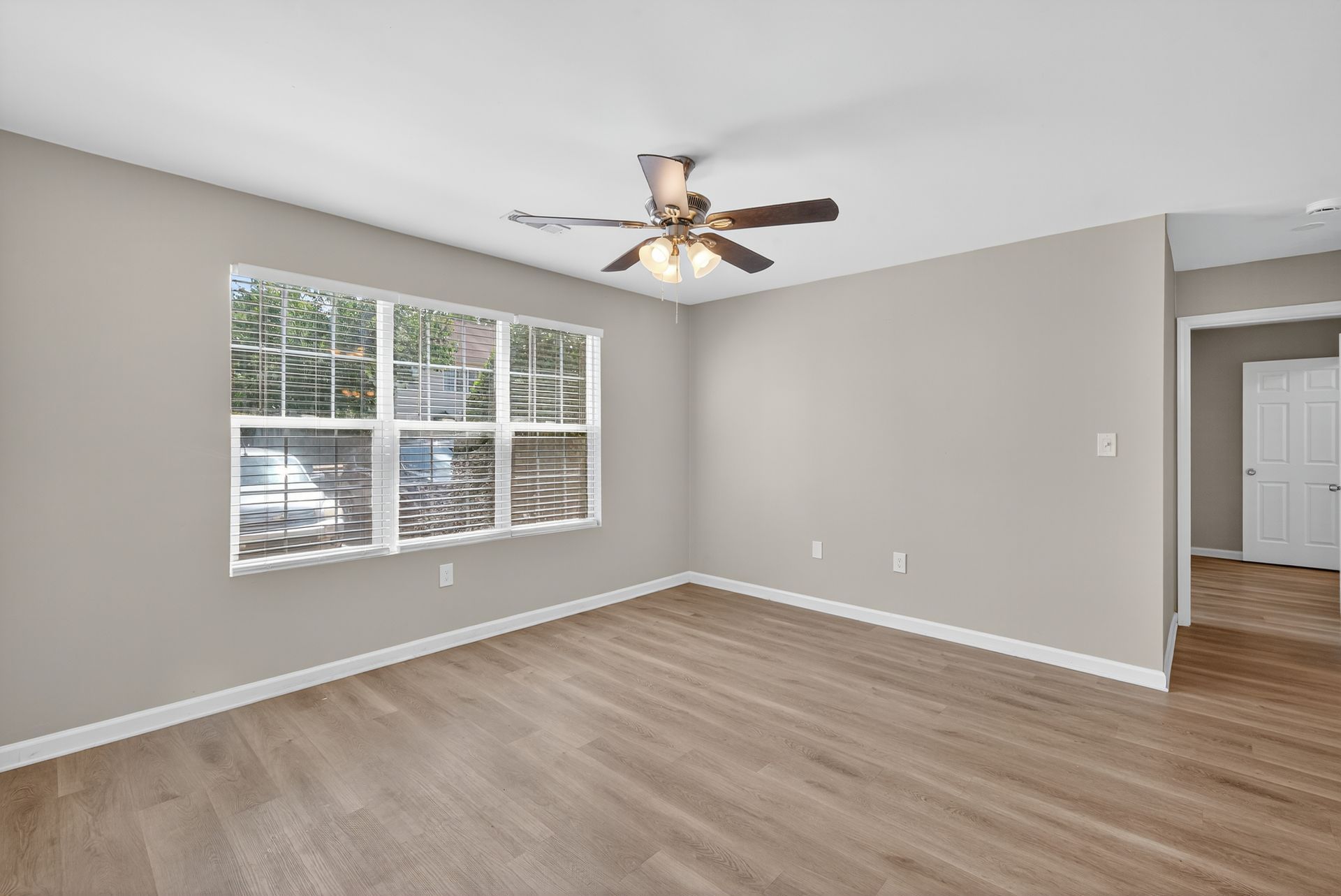 Empty bedroom with light gray walls, wood floors, a ceiling fan, and a window with blinds.