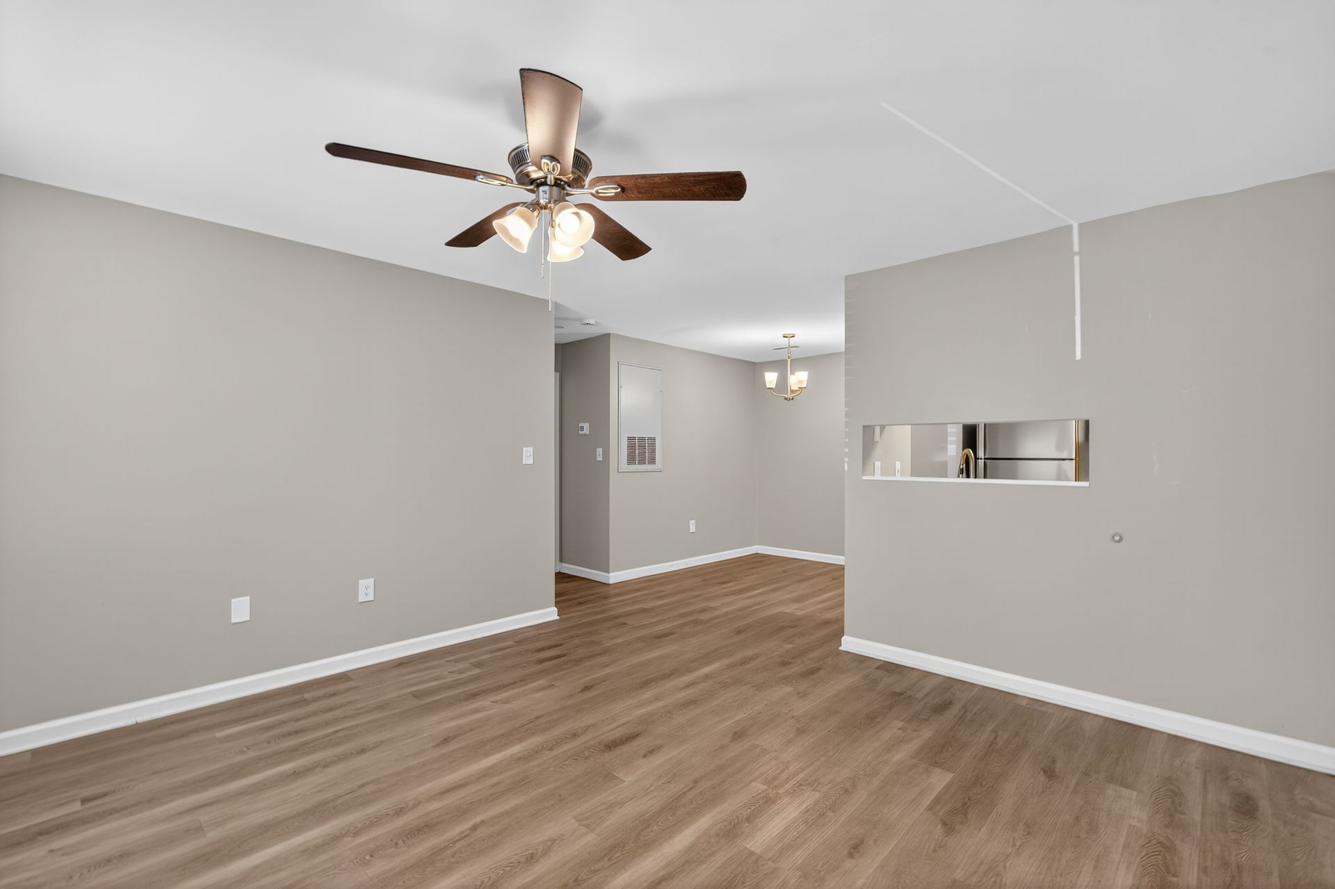 Empty gray living room with wood floor, ceiling fan, and pass-through opening to kitchen