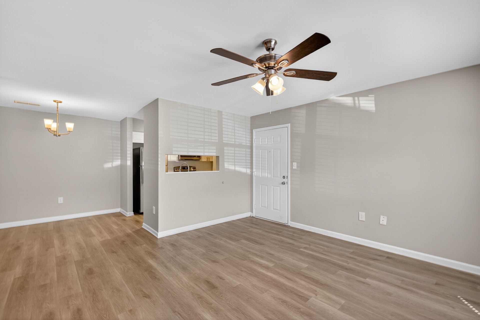 Empty living room with gray walls, wood floors, ceiling fans, and a white closet door