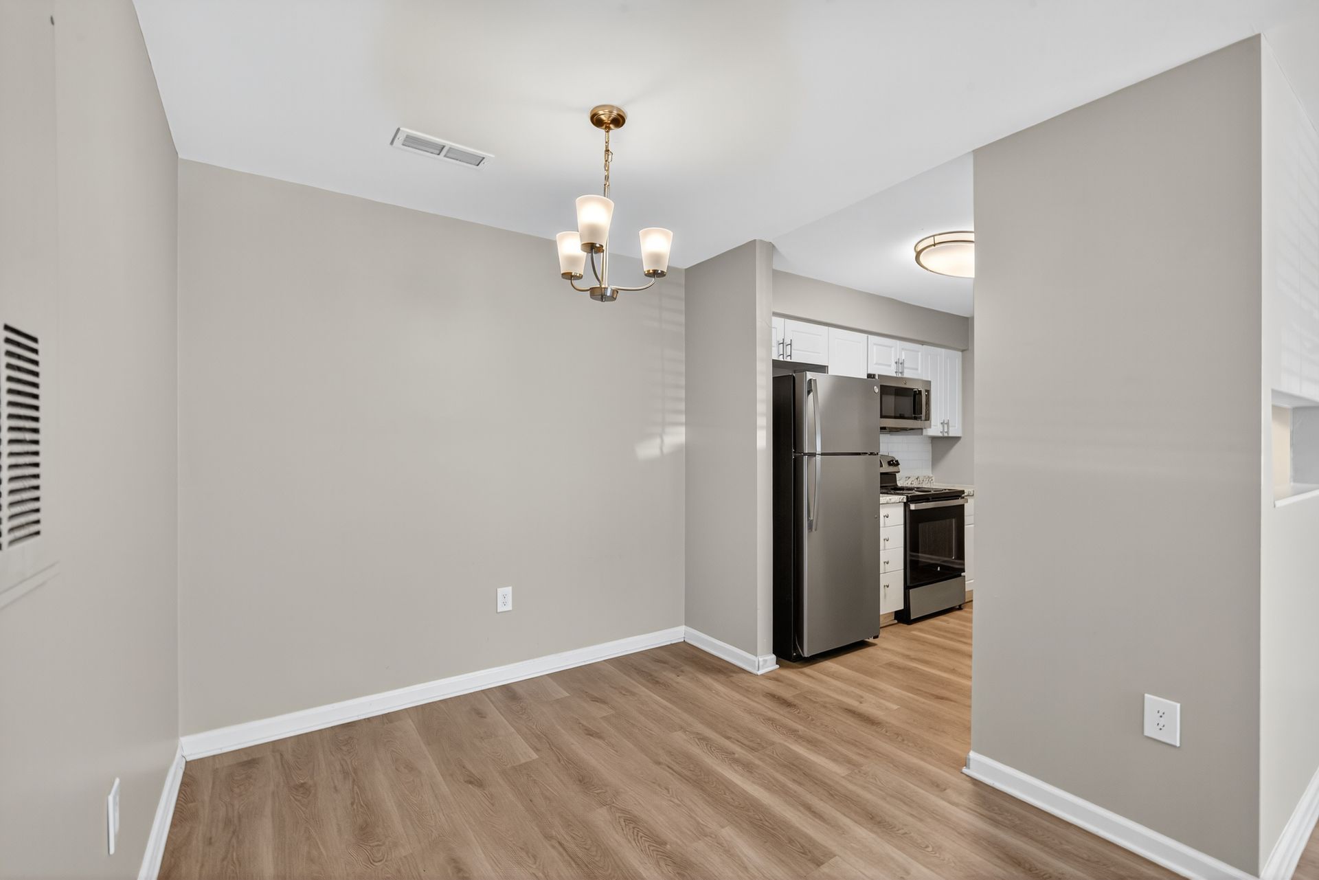 Empty dining area with gray walls, wood-look flooring, and a view into the kitchen with stainless steel appliances