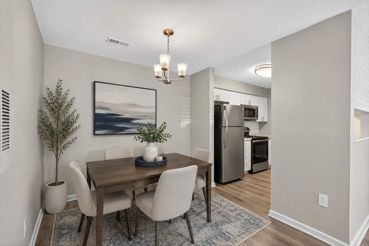 Dining area with round table, beige chairs, wall art, and open view into a kitchen and hallway.