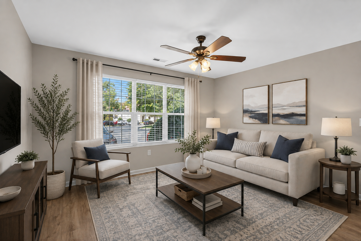 Bright living room with beige sofa, chair, coffee table, large windows, and ceiling fan in neutral tones