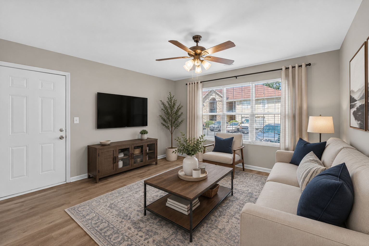 Bright living room with beige sofa, wall TV, coffee table, and large window with city view