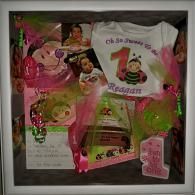 Pink and white birthday gift basket with a personalized shirt and assorted treats inside a framed box