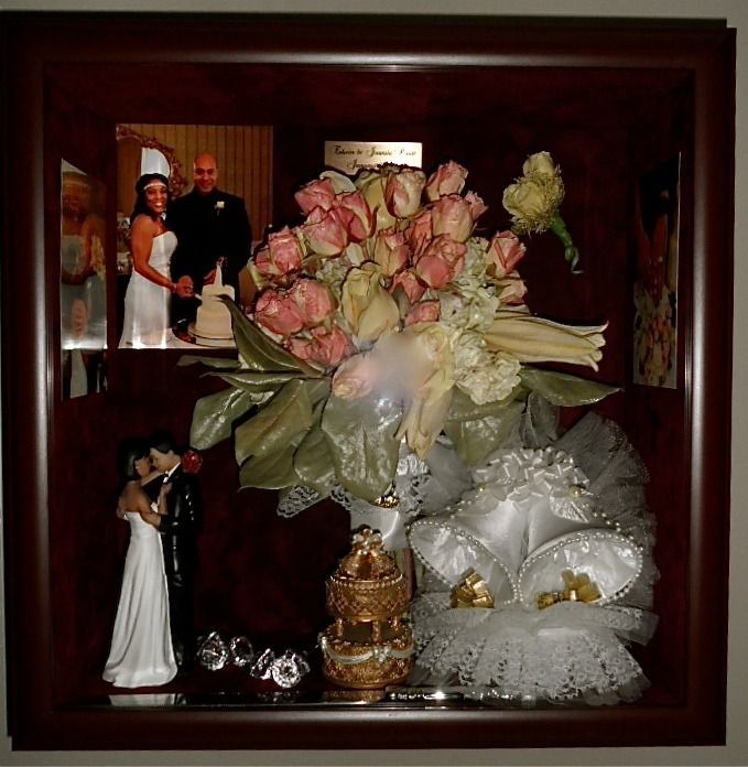 Wedding keepsake display with bouquet, bride and groom photo, figurine, and white decorative pillows in a shadow box