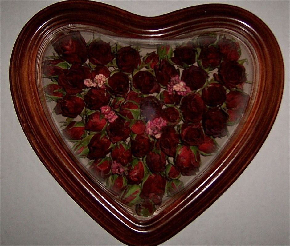 Heart-shaped wooden frame filled with red roses and greenery on a wall