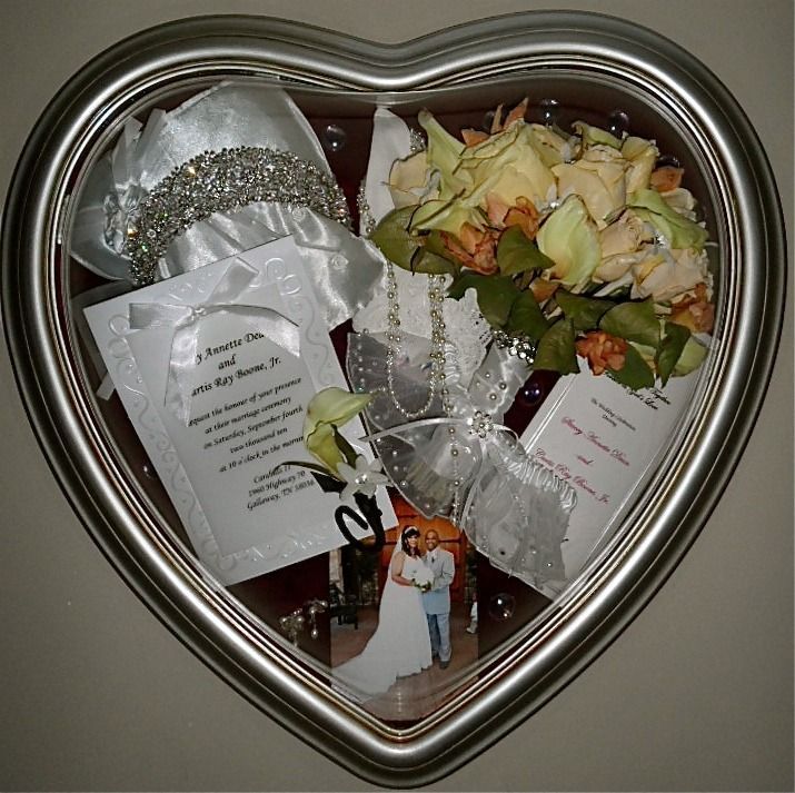 Heart-shaped silver frame holding wedding keepsakes, ribbons, and a small wedding photo collage.