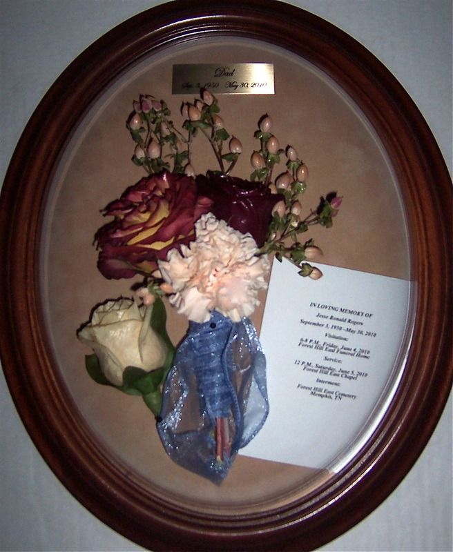 Framed oval floral arrangement with a card and ribbon on a beige background