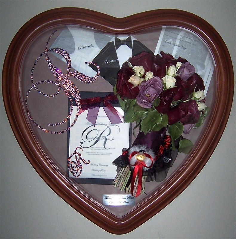 Heart-shaped shadow box with purple roses, ribbon, and decorative keepsakes against a white background