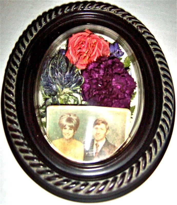 Oval framed memorial photo with flowers and a small vintage portrait inside
