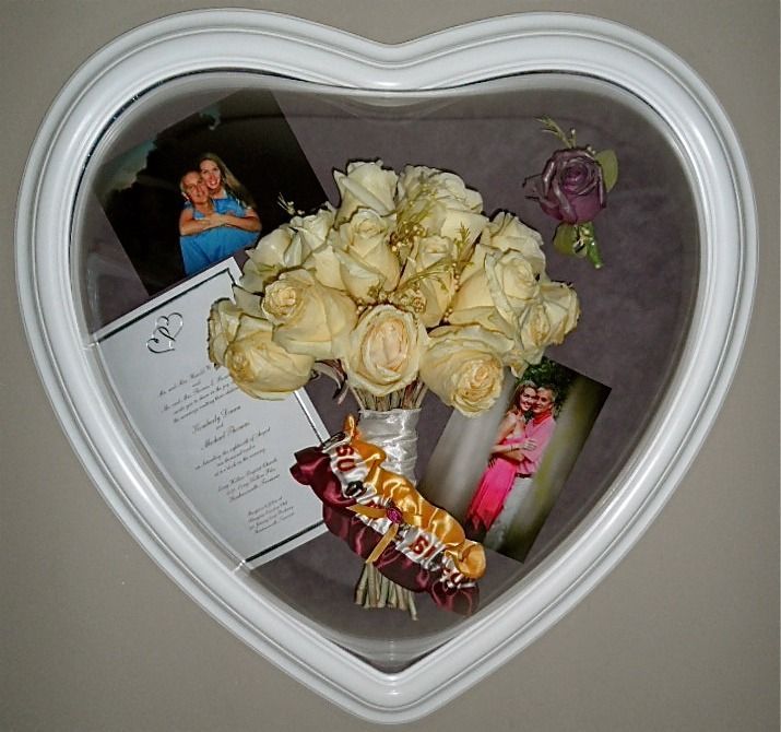 Heart-shaped shadow box with cream roses, photos, and a ribbon on a gray wall