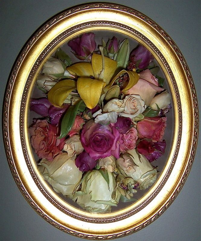 Oval gold frame holding a bouquet of pink, white, yellow, and green flowers on a dark background