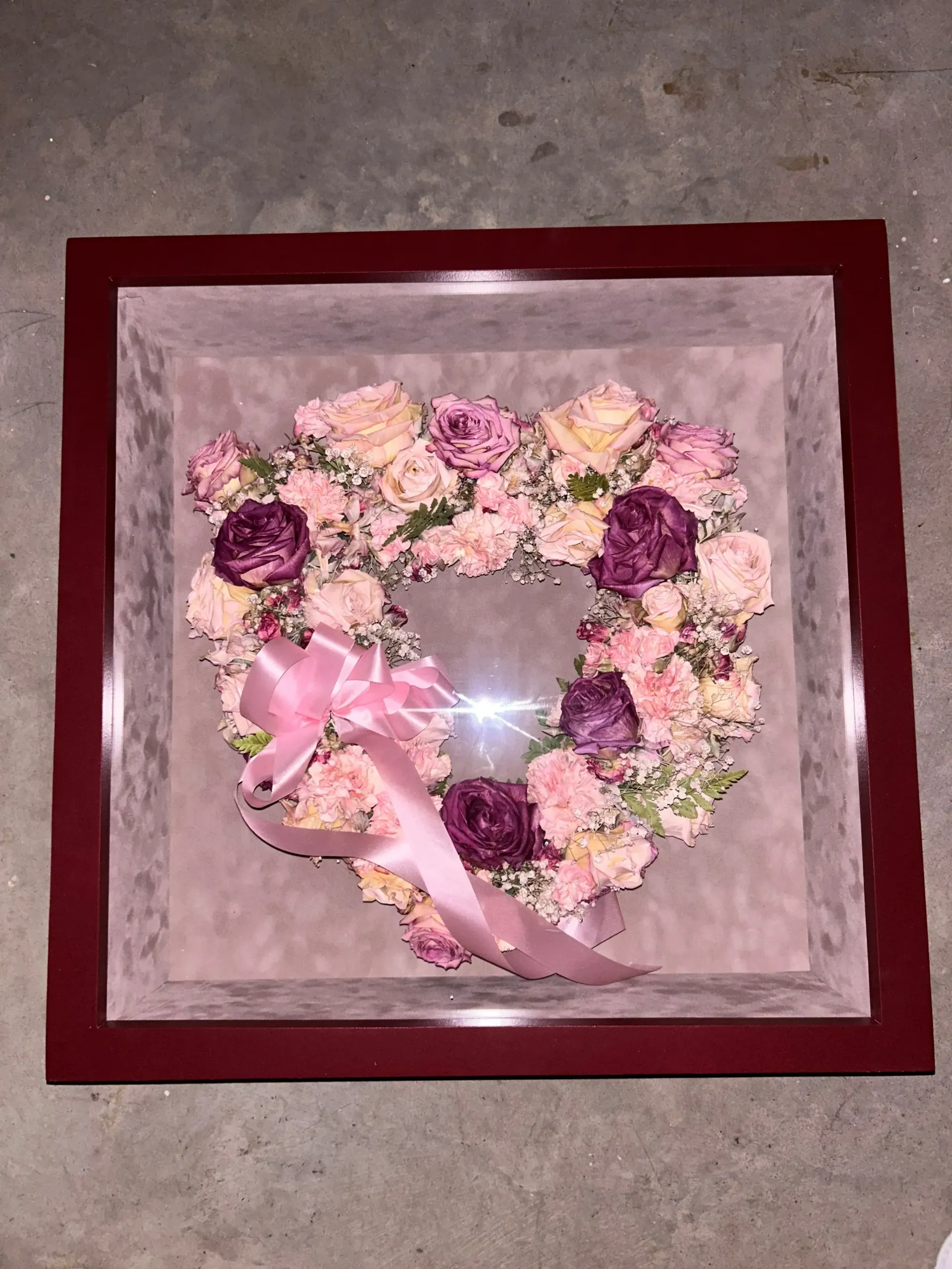 Heart-shaped pink and purple flower arrangement in a burgundy shadow box frame