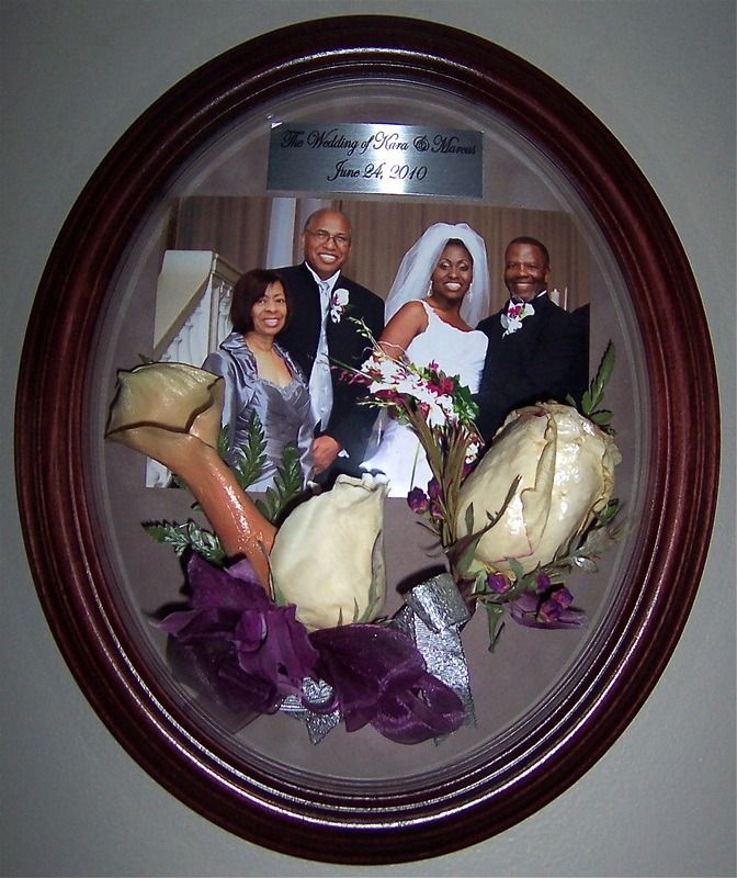 Framed wedding photo with bride and groom holding bouquets, flanked by two guests.