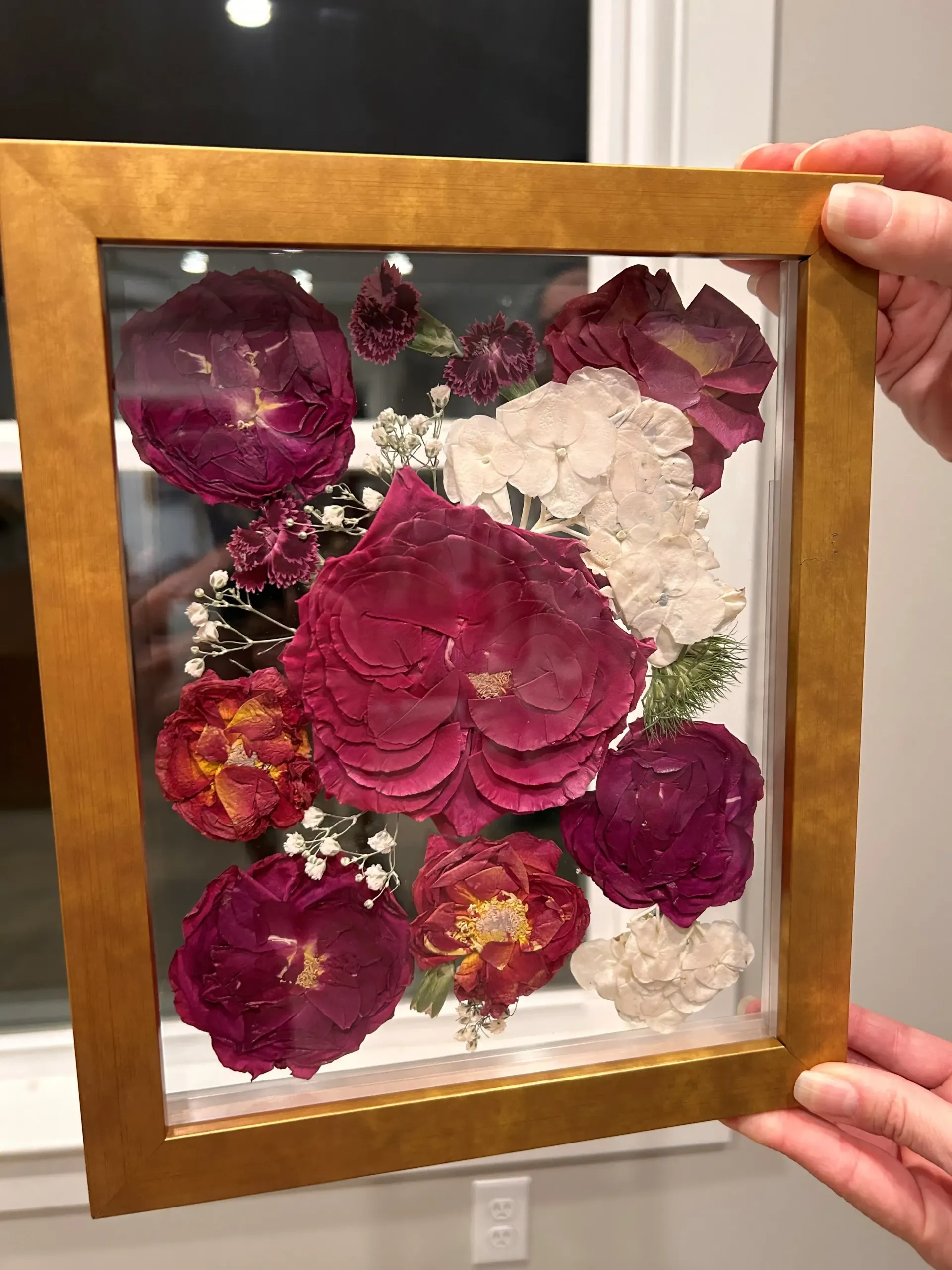 Framed pressed flowers in magenta, purple, and white held by two hands
