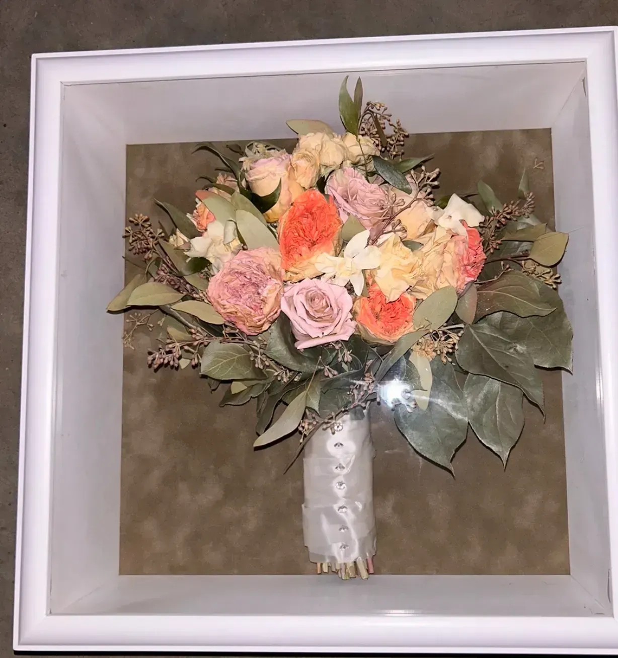 Framed bouquet of pastel artificial flowers in white wrap against a brown background