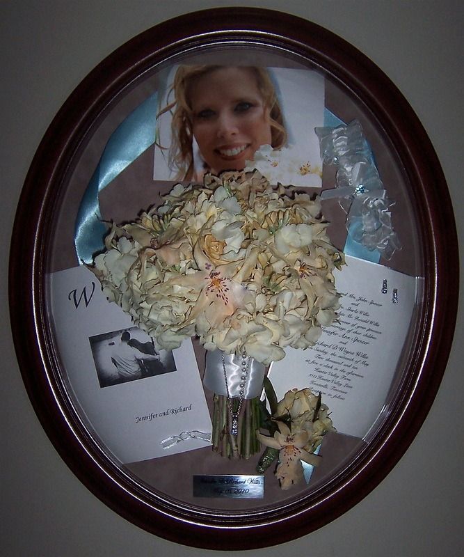 Framed memorial display with a bouquet, magazine clippings, and a portrait photo inside a dark oval frame