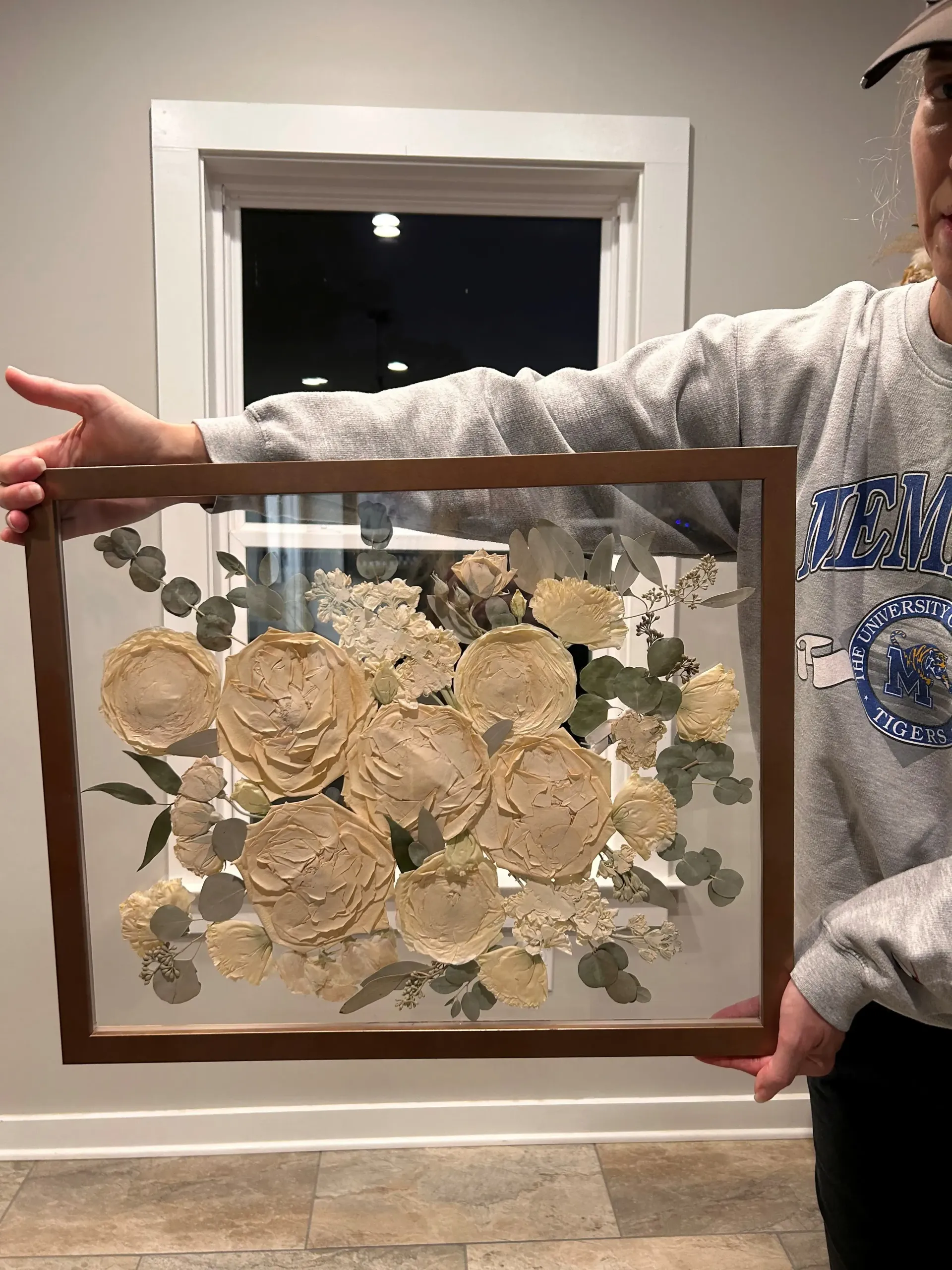 Framed pressed flowers held up indoors in front of a window