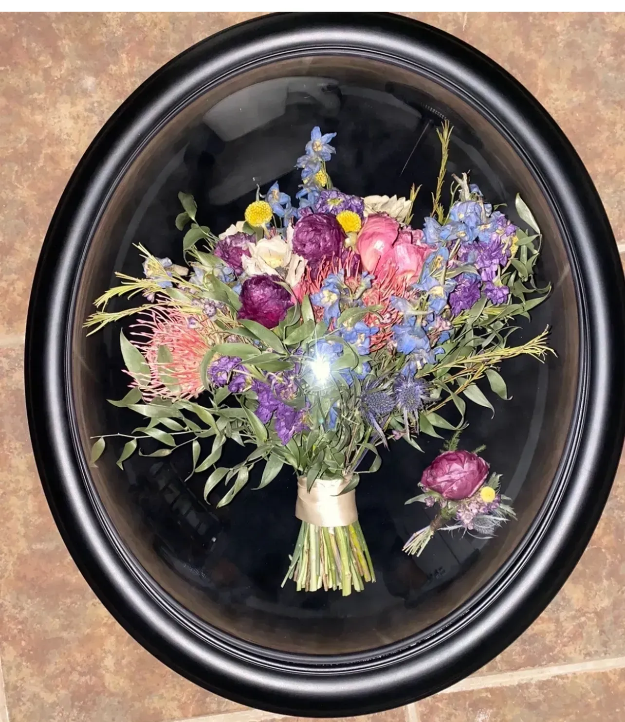 Oval black frame with a colorful bouquet of dried flowers on a dark background