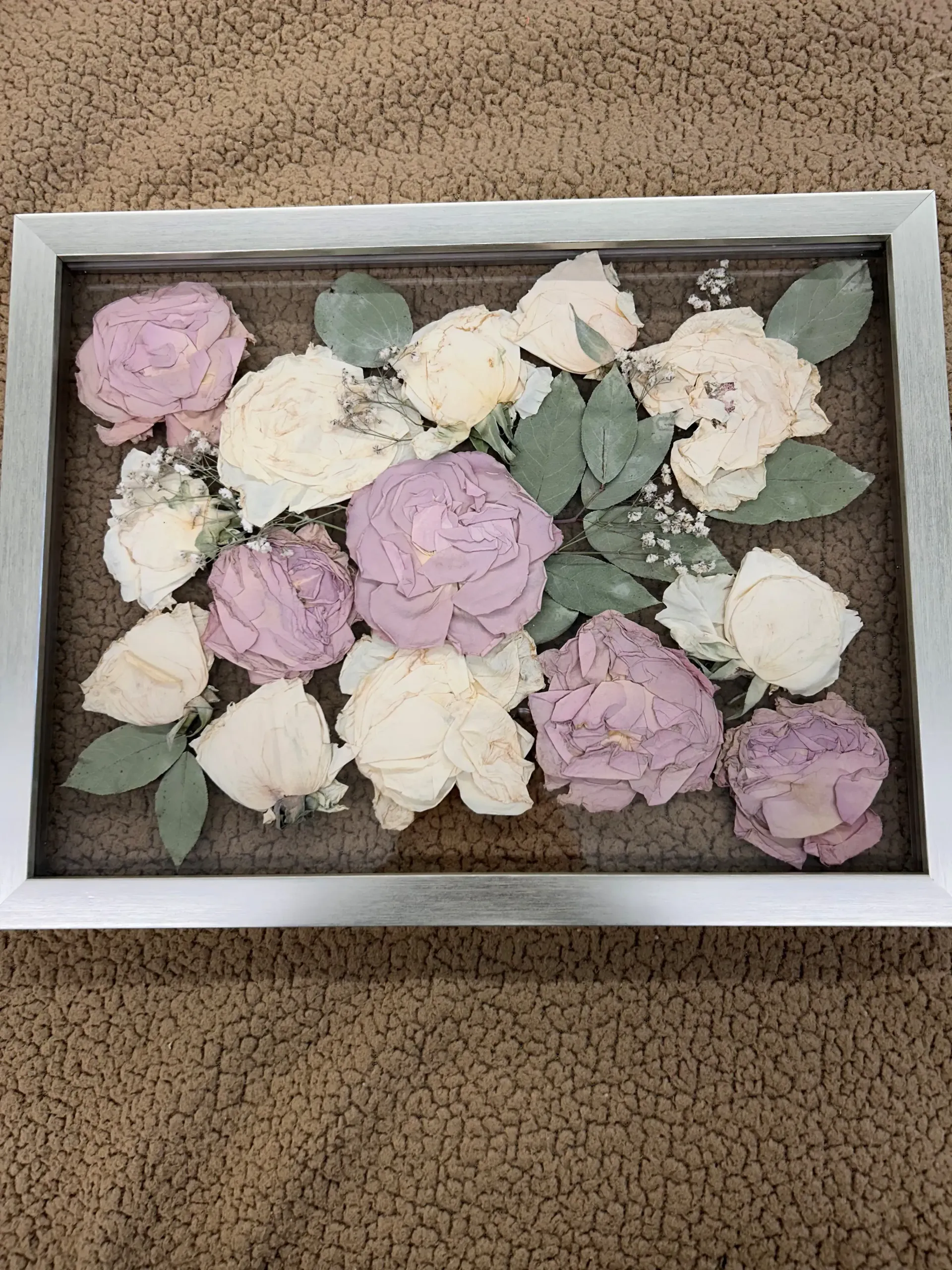 Box of pastel pink and white flowers with green leaves arranged on a brown textured surface