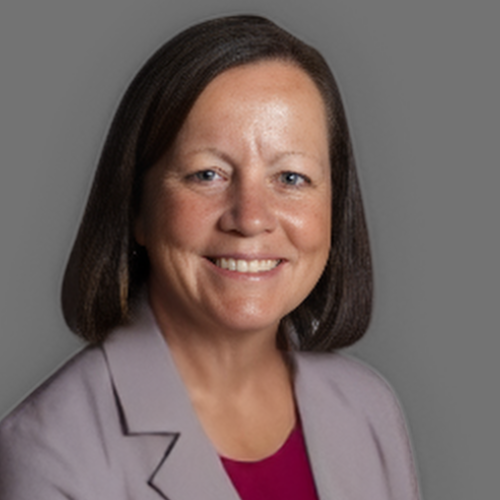 A woman wearing a purple jacket and a pink shirt is smiling for the camera.