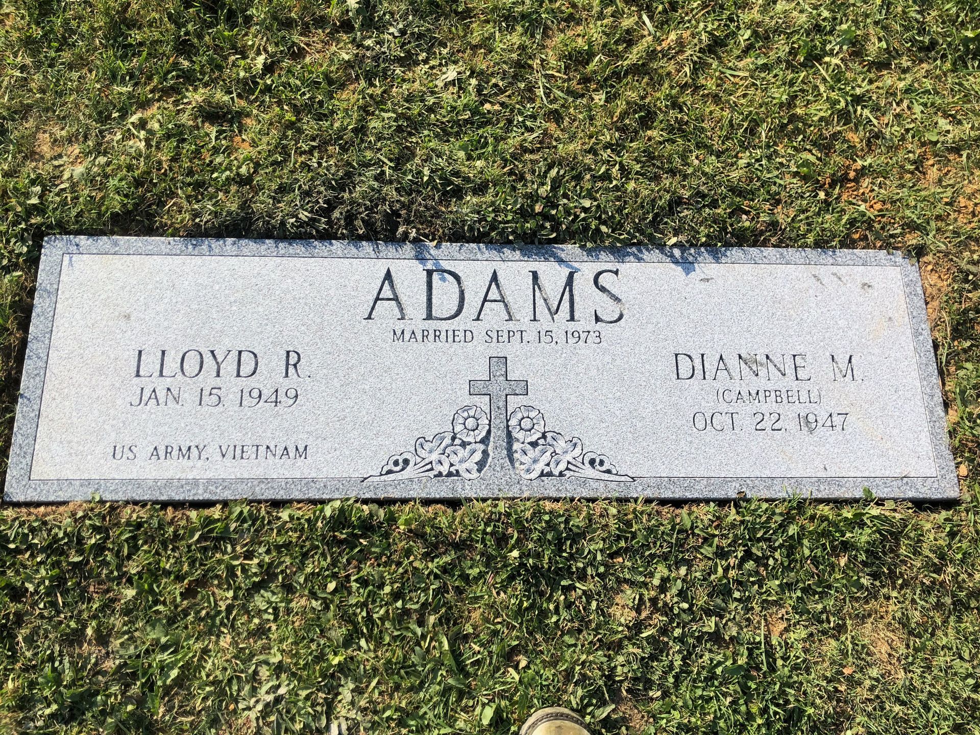 Gravestone for Adams with engraved names and dates, set in a grassy cemetery plot.
