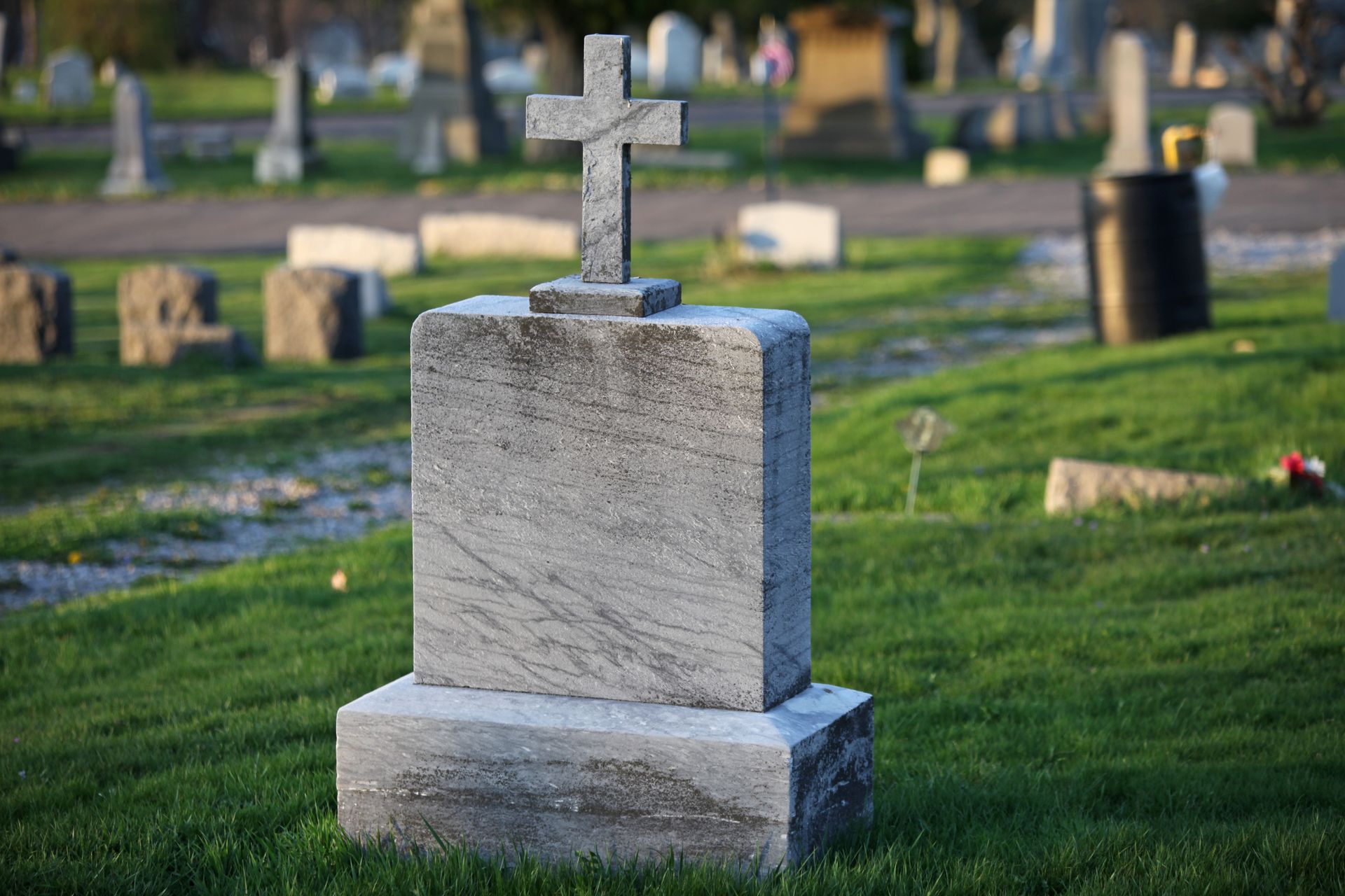 A cemetery featuring a prominent gray marble tombstone with a cross on top in the foreground.