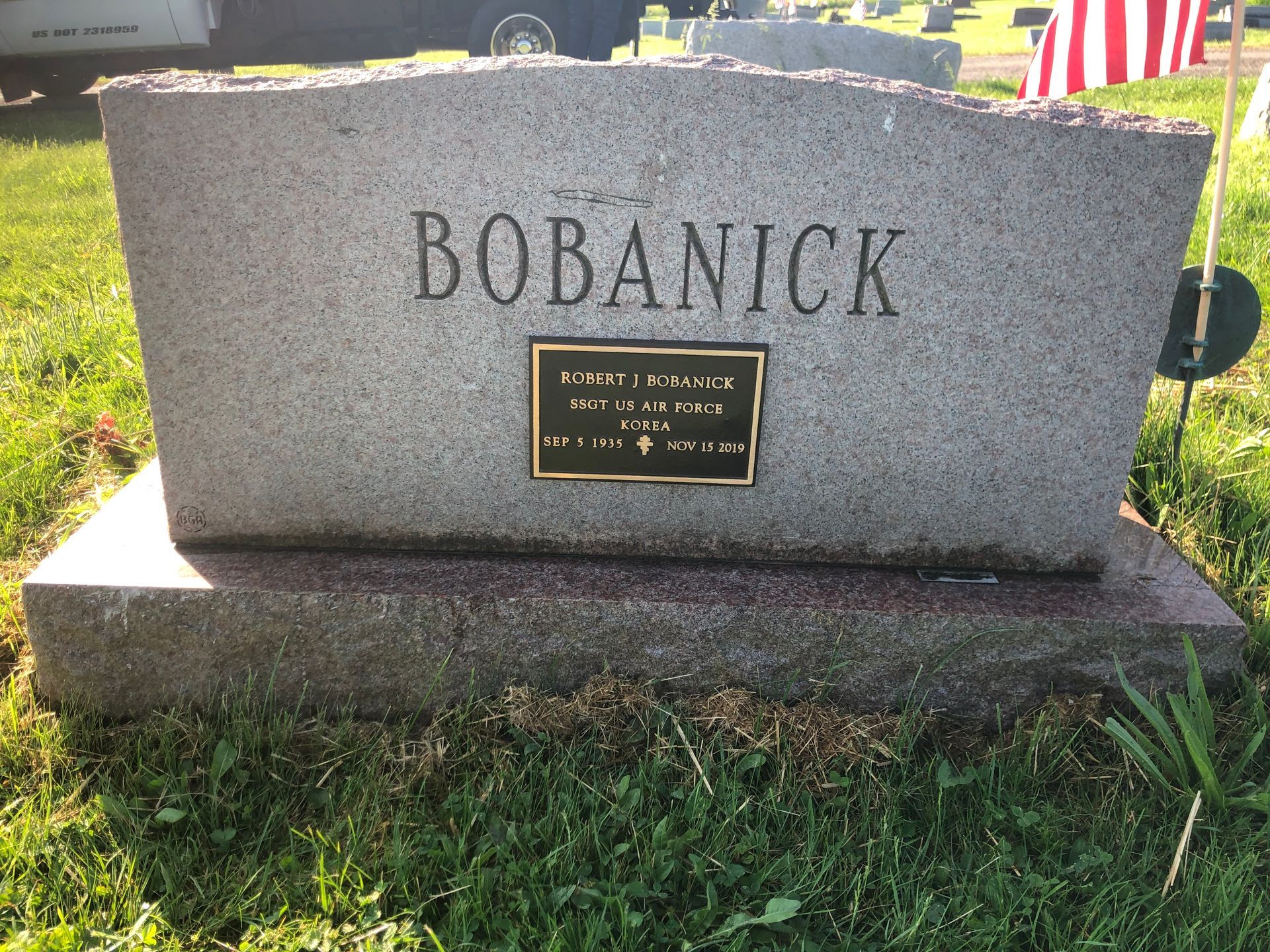 Gray granite BOBANICK gravestone with a plaque, set on a grassy cemetery plot.