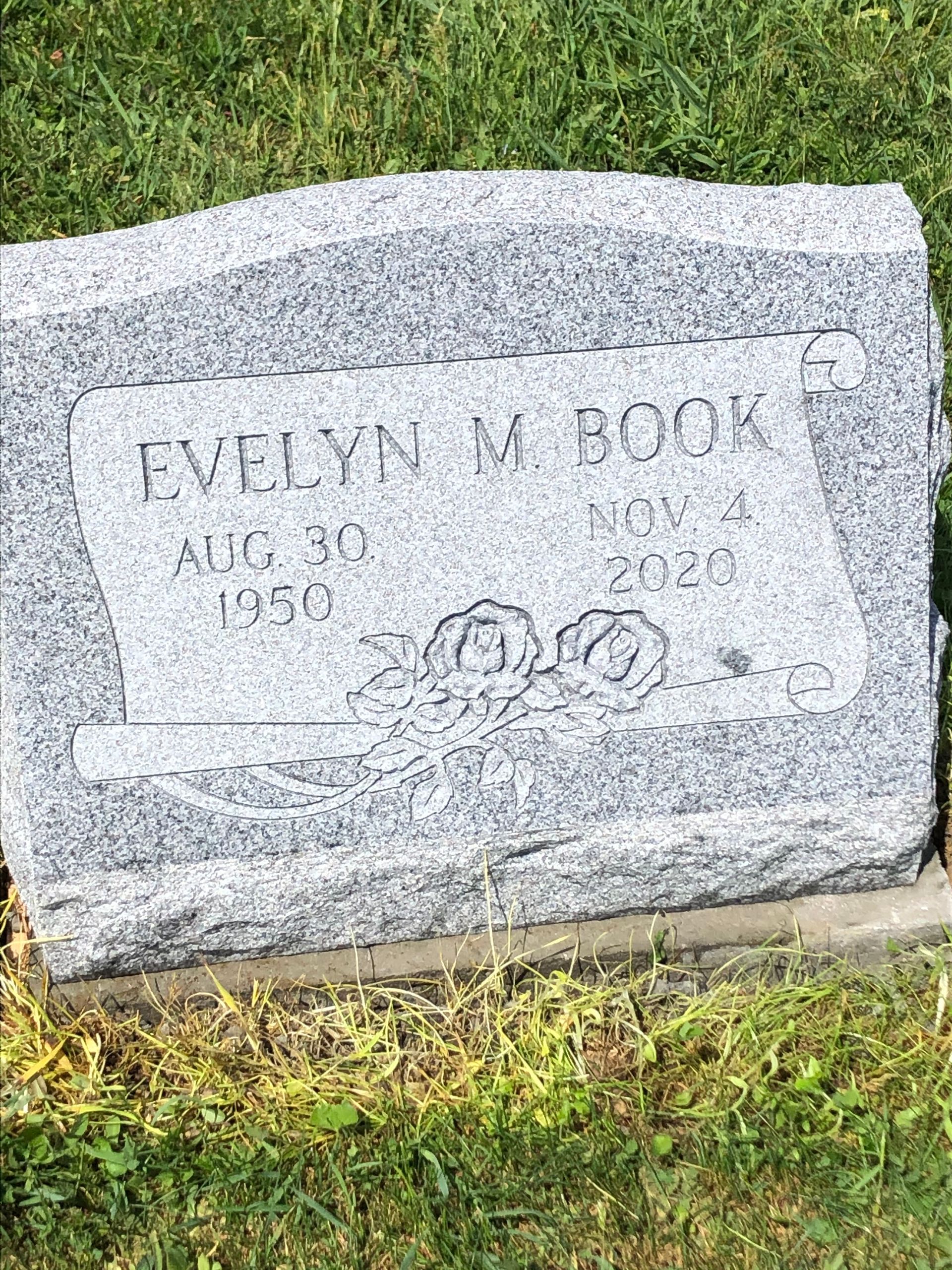 Gravestone in grass inscribed “Evelyn M. Book,” with dates and a decorative etched design