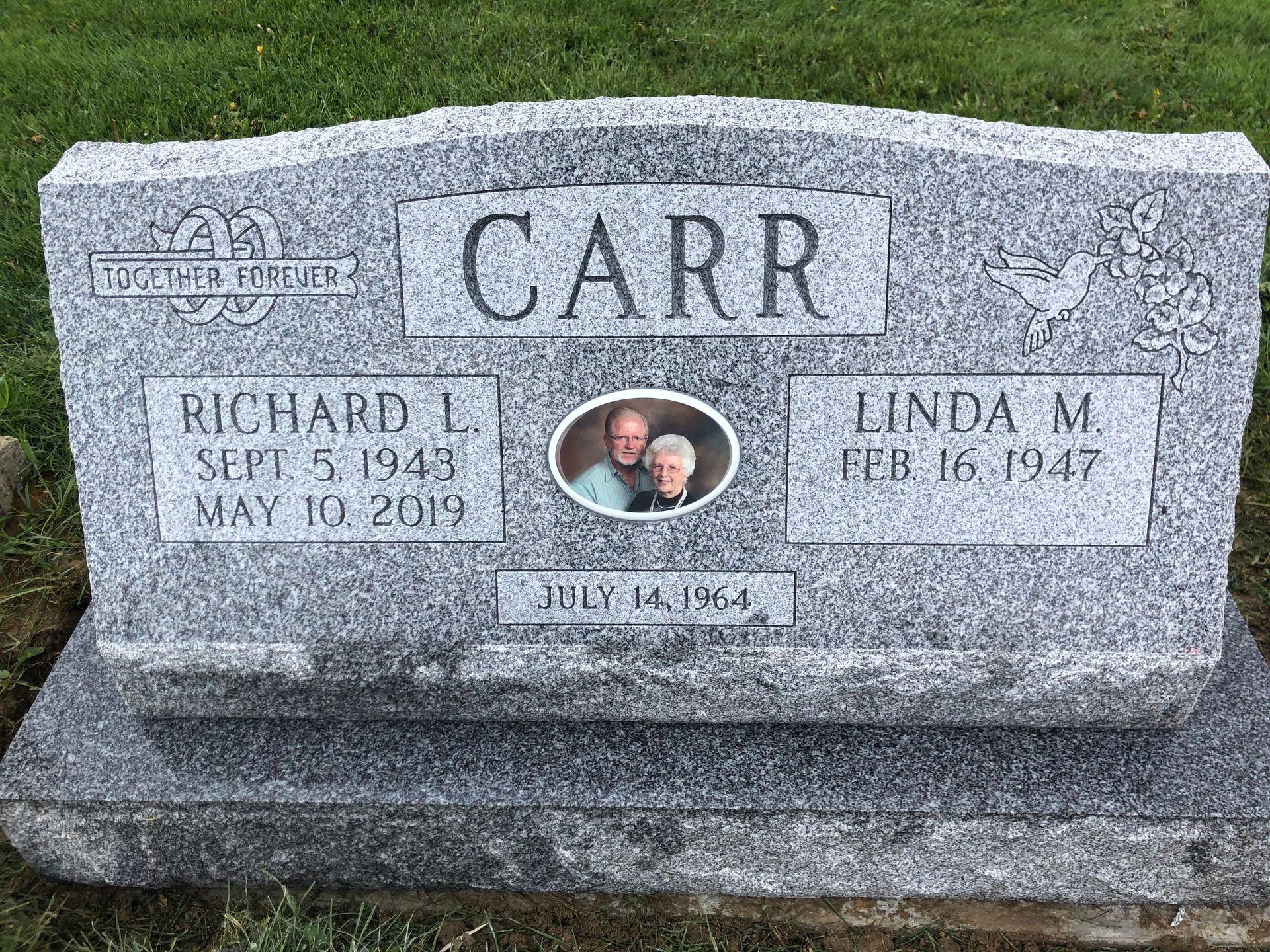 Gray memorial gravestone engraved “CARR” with two oval portraits and names in a grassy cemetery.