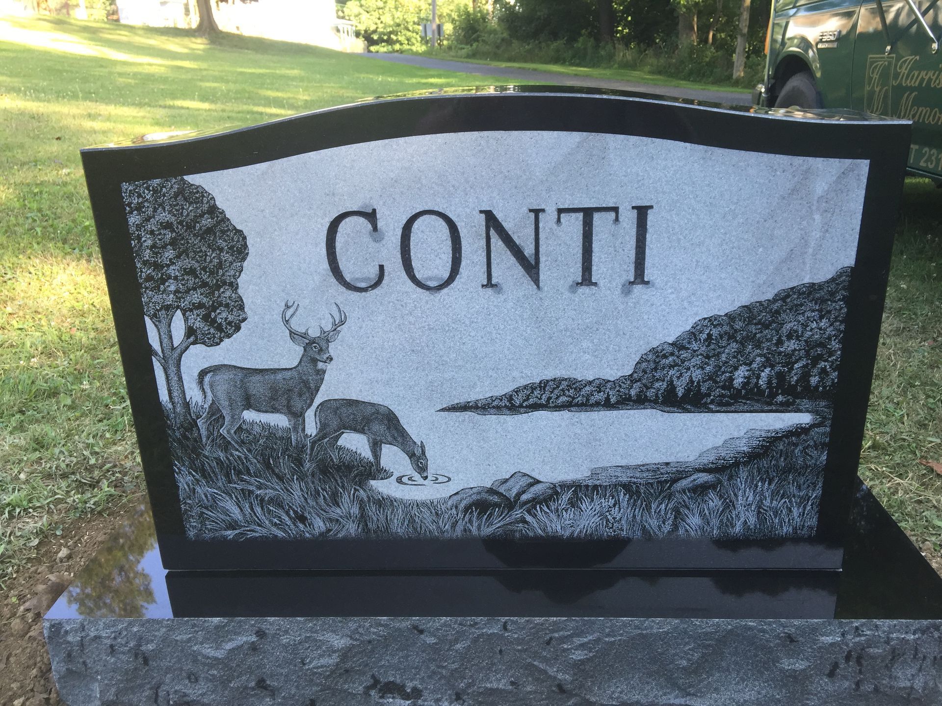 Gravestone with the name CONTI, featuring a deer and lakeside landscape engraving.