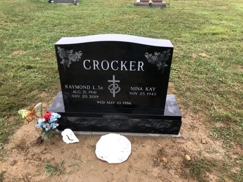 Black granite gravestone with flowers in a grassy cemetery, marked “Crocker” and cross emblem