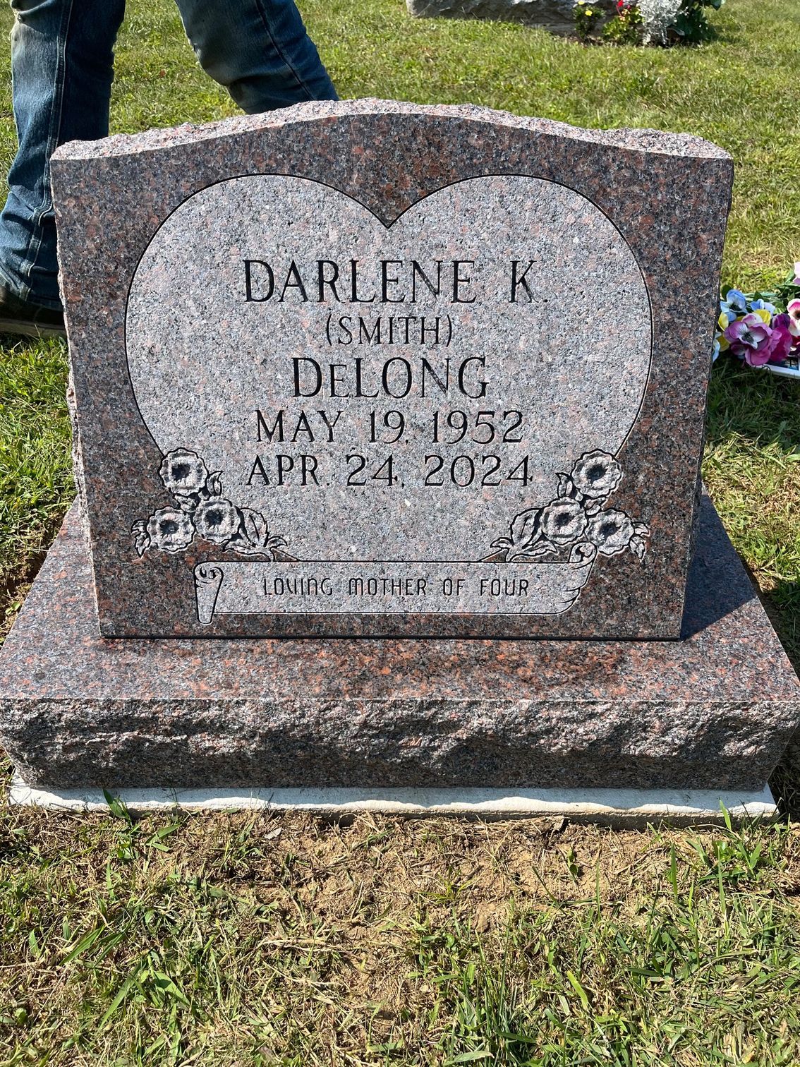 Heart-shaped gray gravestone with engraved names and dates in a grassy cemetery.