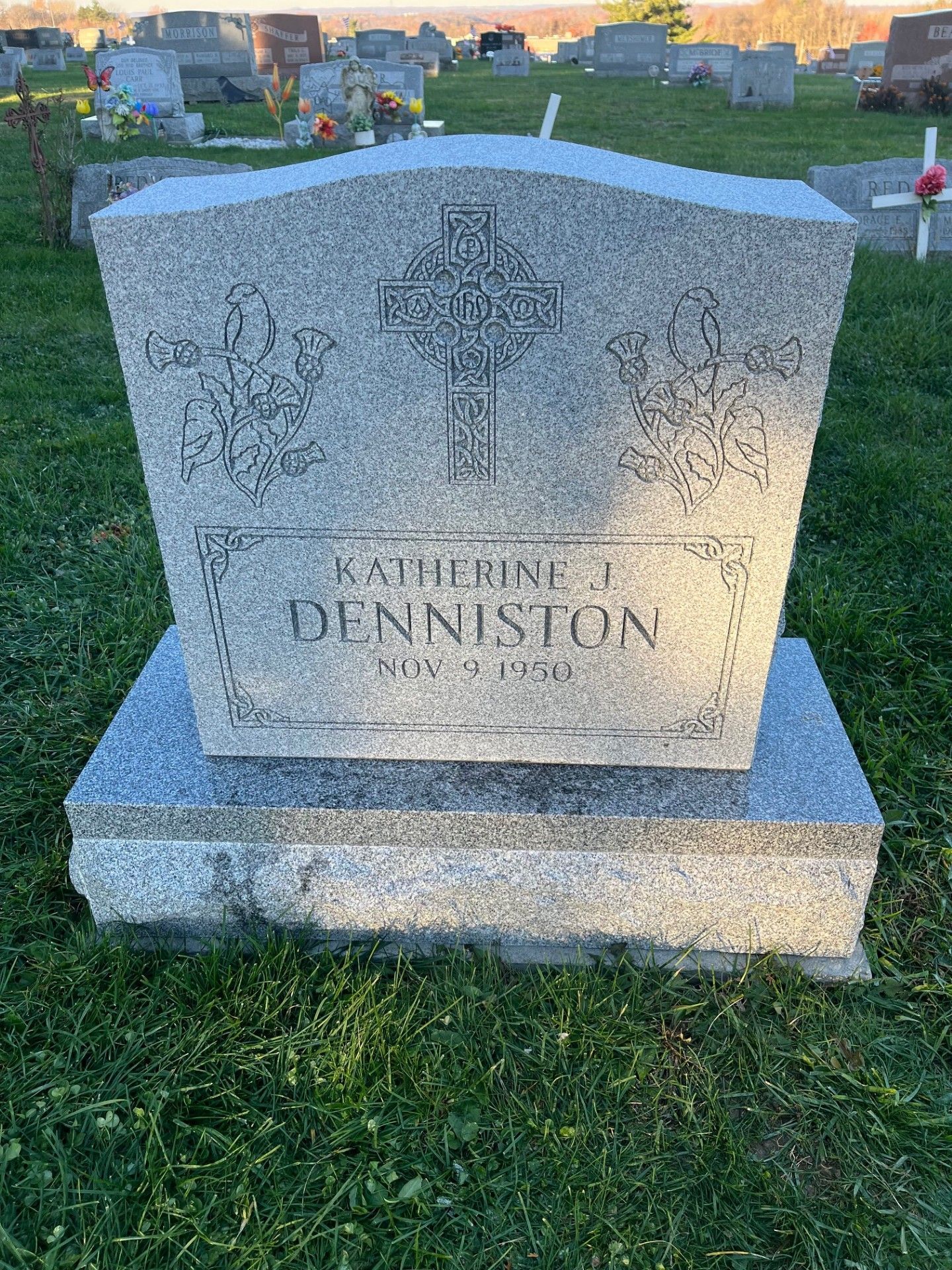 Gravestone with a cross engraving in a grassy cemetery at sunset