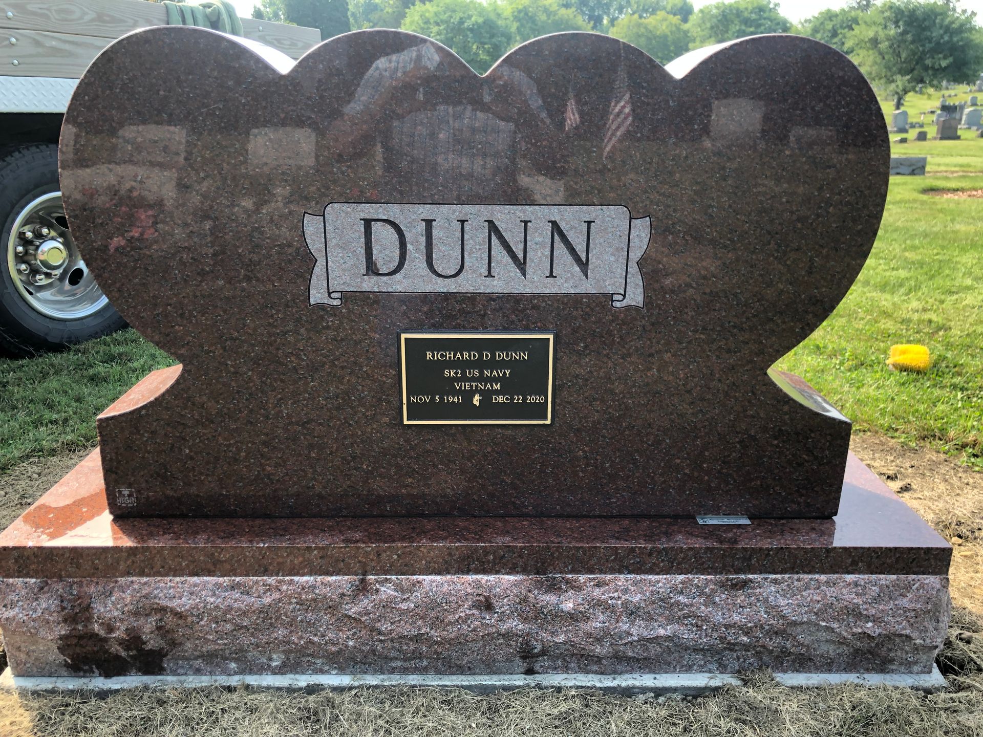 Dark granite gravestone with scalloped top and “DUNN” engraved on a white plaque.