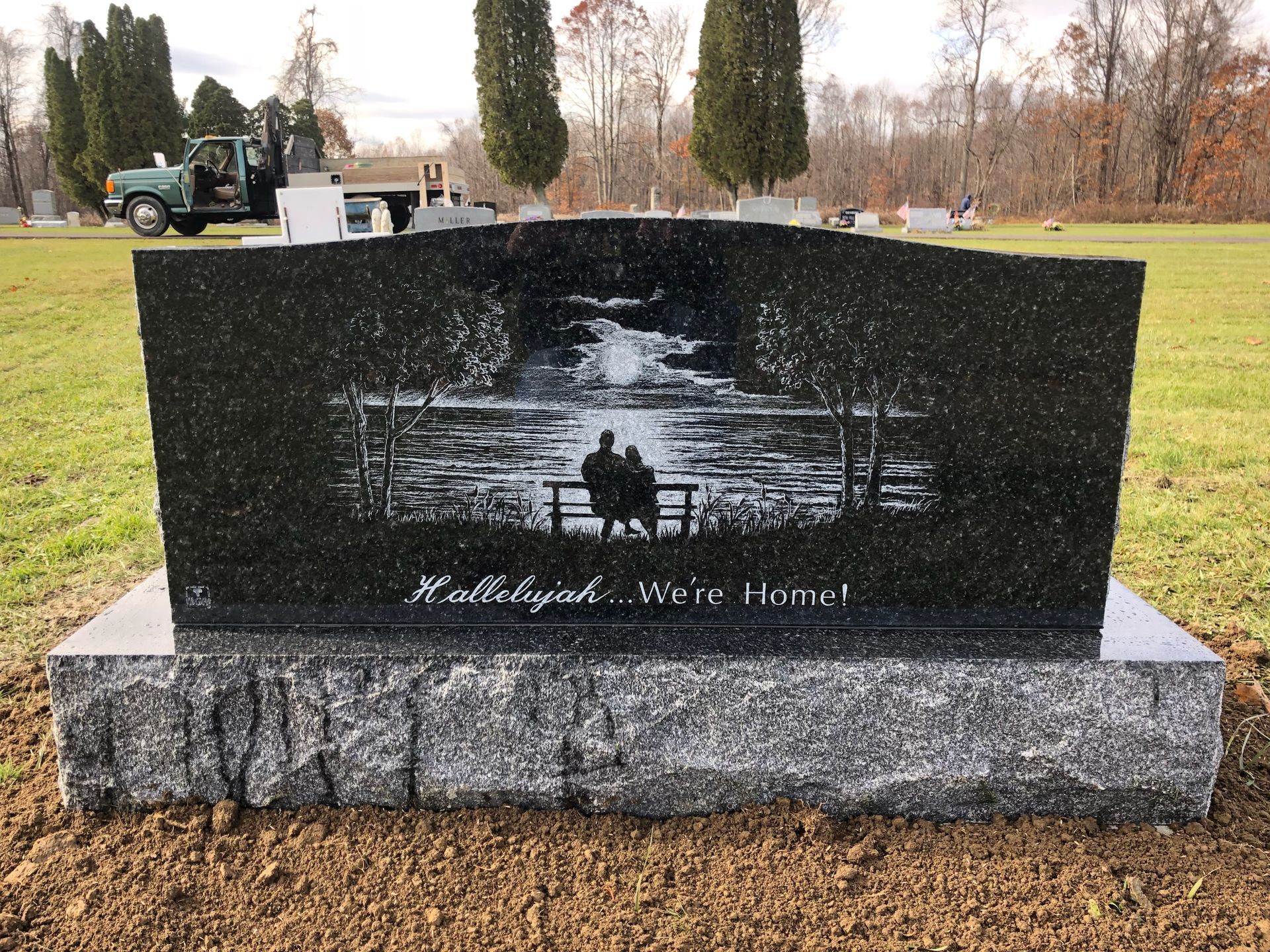Black granite memorial bench with etched river scene in a grassy cemetery