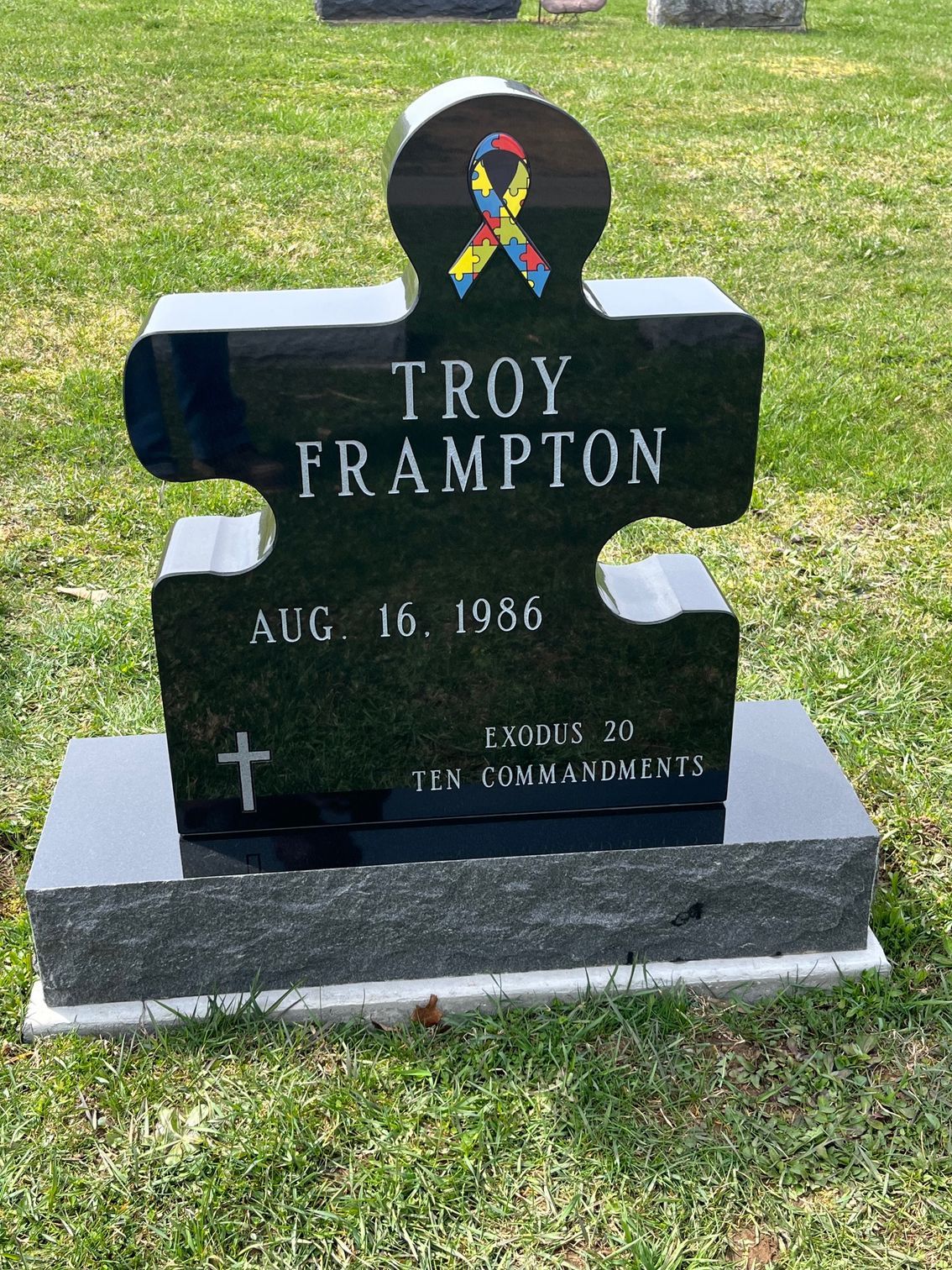 Black gravestone in a grassy cemetery with rainbow ribbon and the name Troy Frampton.