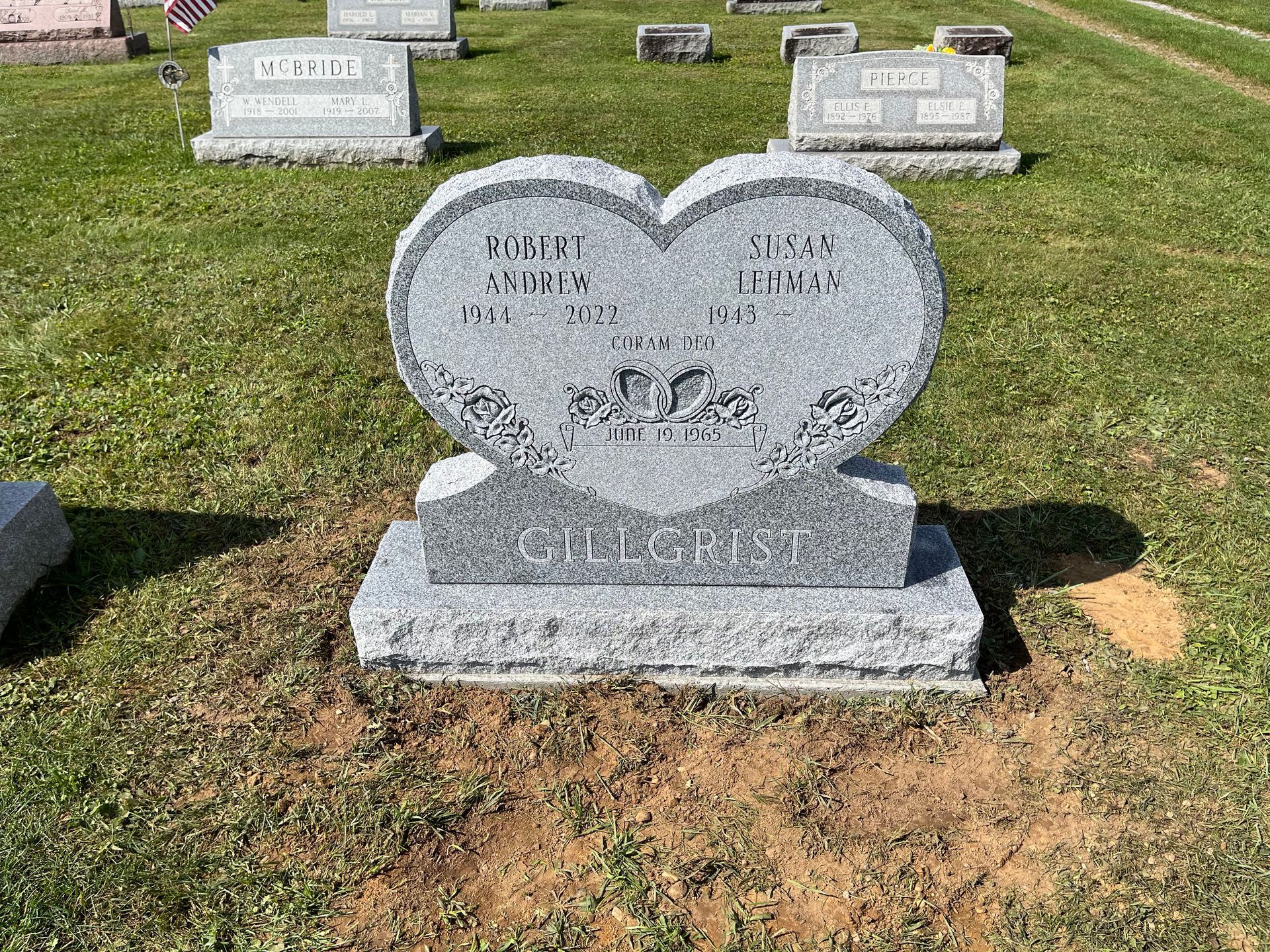Heart-shaped gray granite gravestone in a grassy cemetery with other headstones in the background