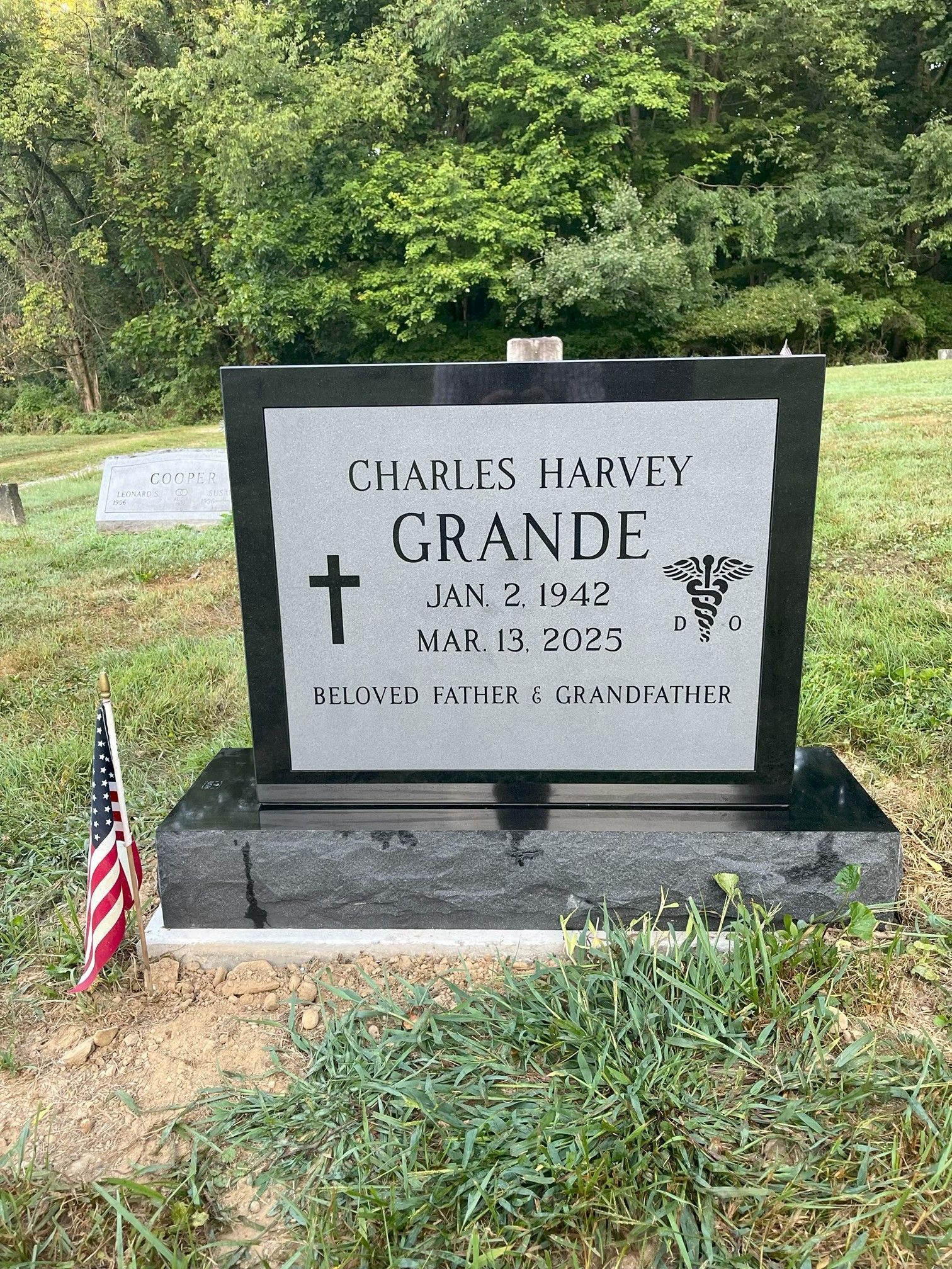 Gravestone for Charles Harvey Grande in a grassy cemetery, with an American flag beside it.