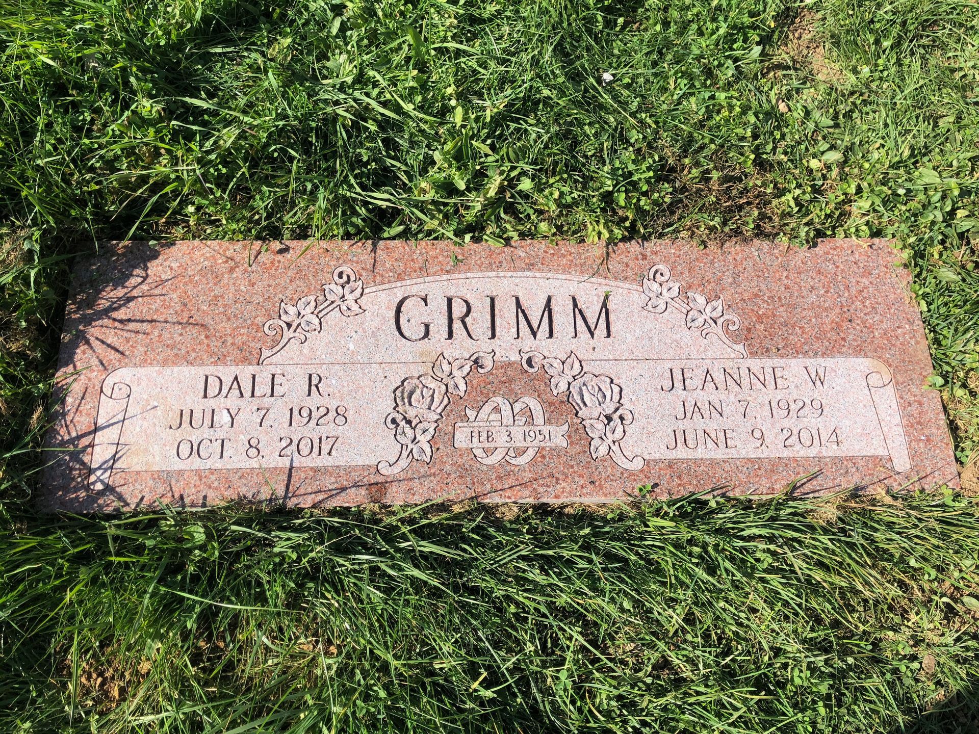 Gravestone on grass with the name GRIMM and two inscription panels on a pink stone marker