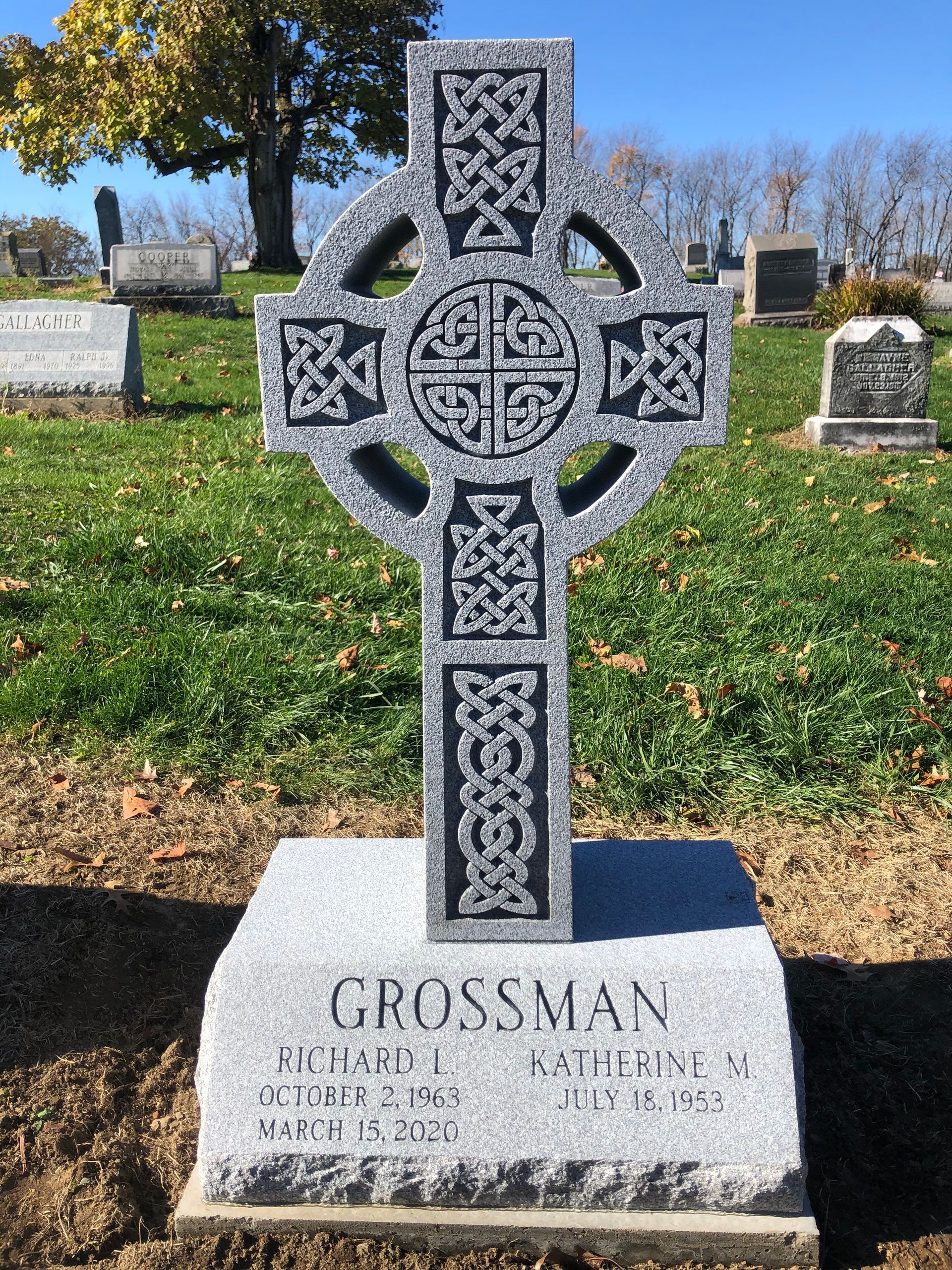 Celtic cross gravestone in a cemetery with autumn trees and grass in the background