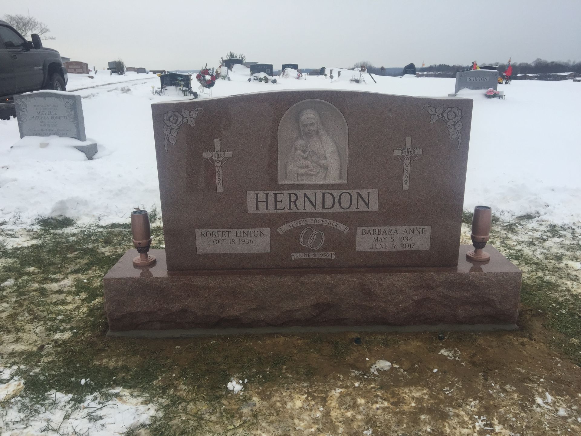 Snowy cemetery with a brown granite headstone marked “HERNDON” and a vase-shaped carving.