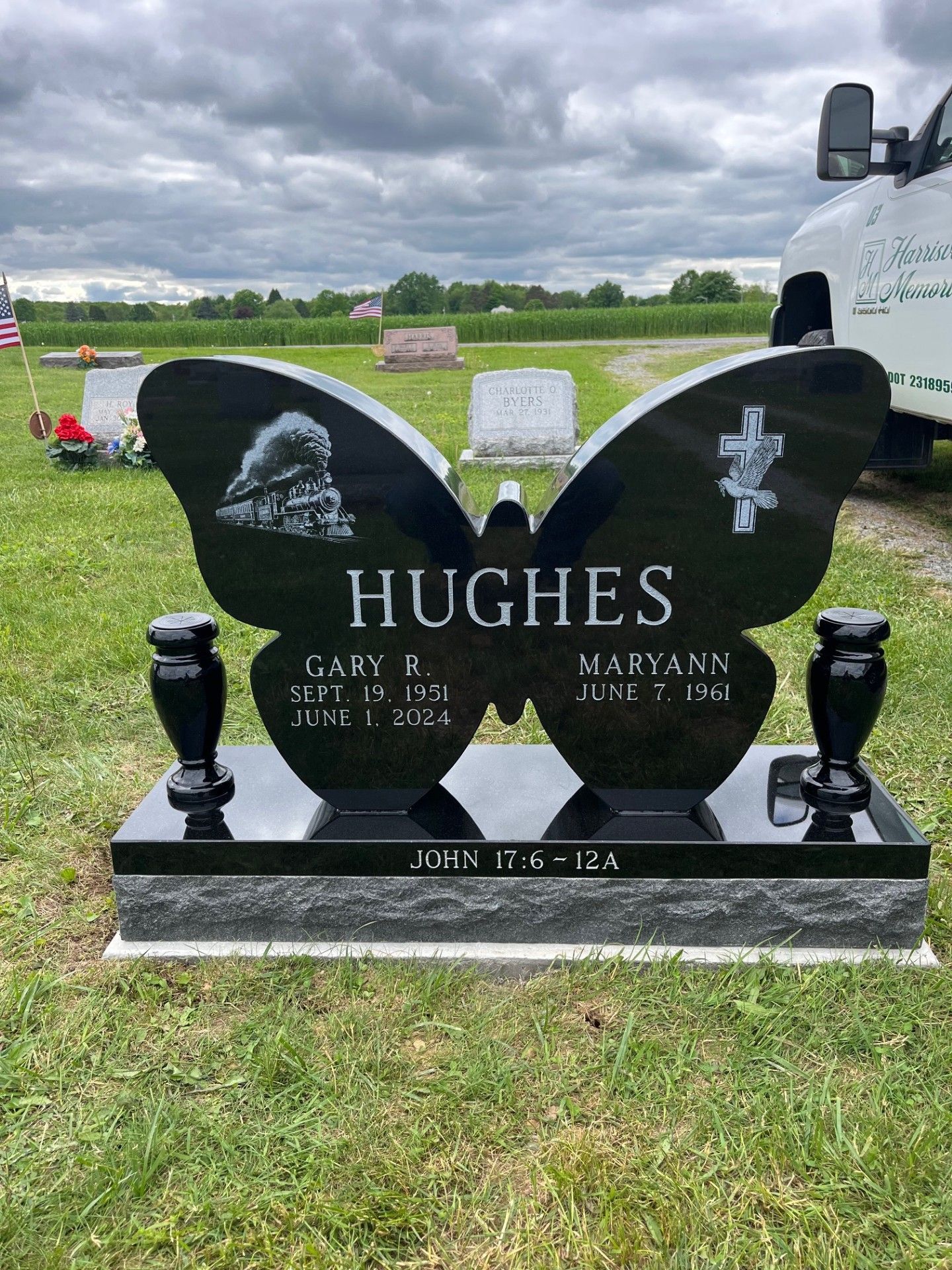 Black Hughes memorial headstone in a cemetery with a white truck parked beside it