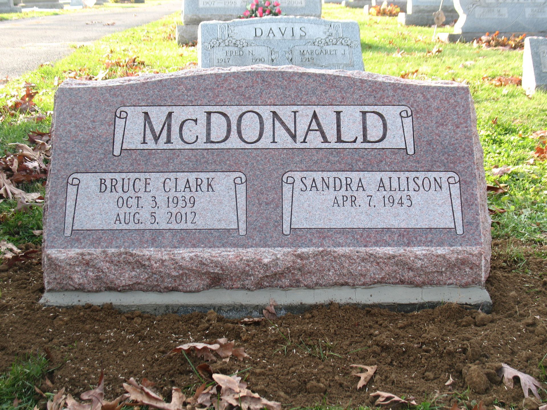 McDonald family gravestone in a cemetery, pink granite marker with engraved names and flowers nearby